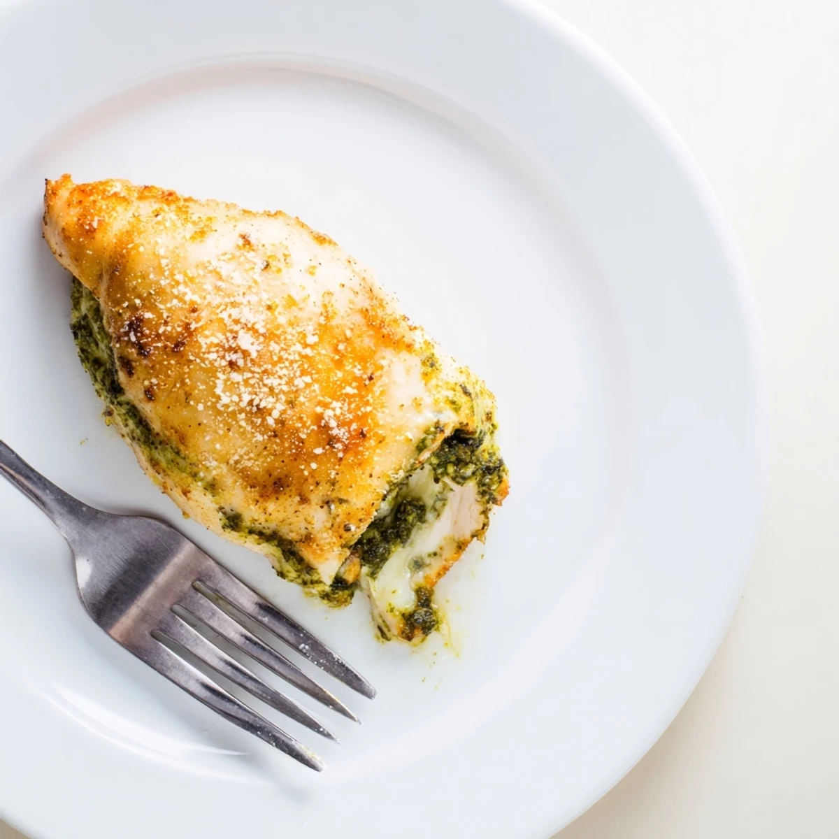 Golden-brown baked Mozzarella & Pesto Stuffed Chicken breasts, stuffed with melted mozzarella and aromatic basil pesto, resting on a white plate.