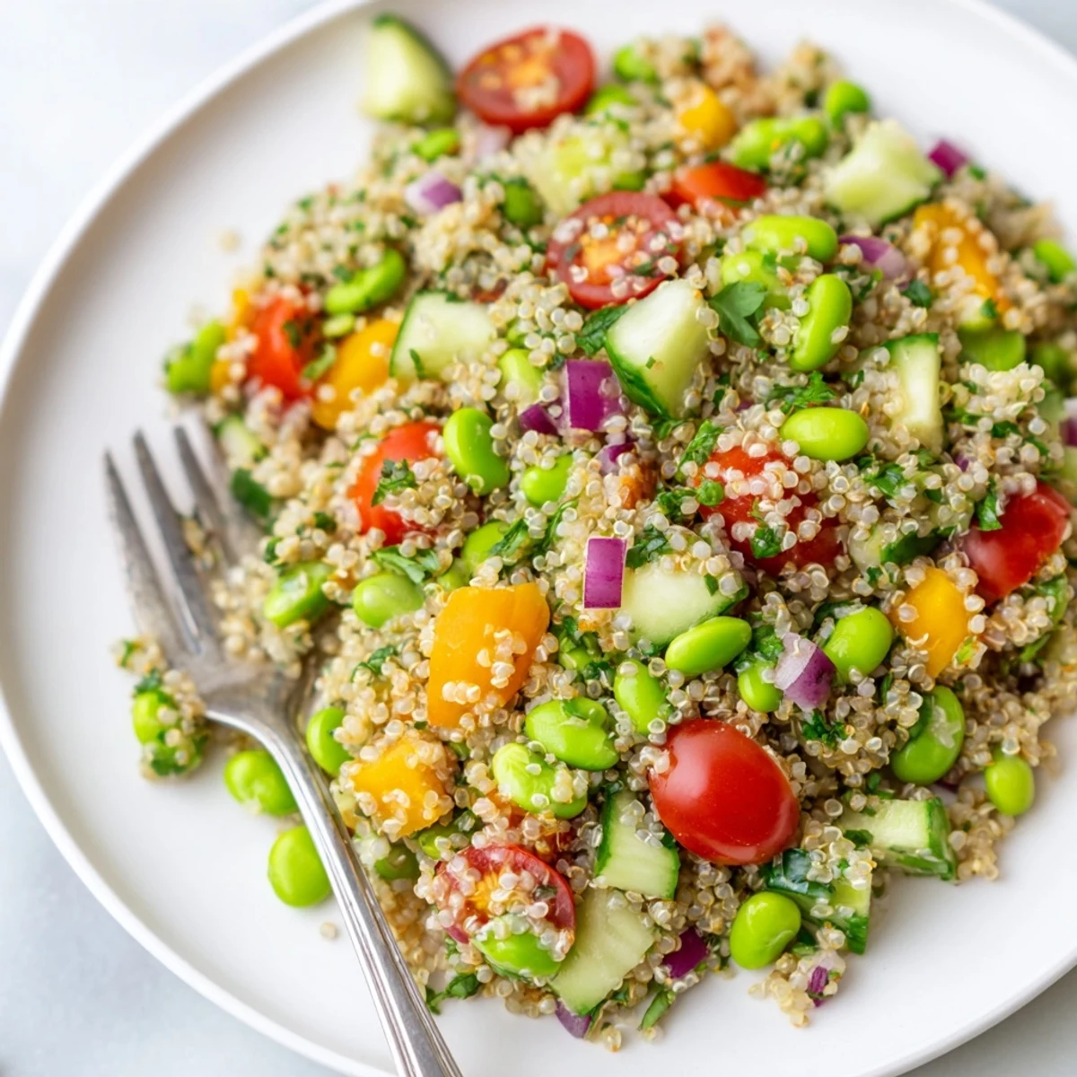 A close-up of the Edamame and Quinoa Salad, showing bright red cherry tomatoes and diced bell pepper mixed with fluffy grains, all tossed in a glistening citrus dressing.  