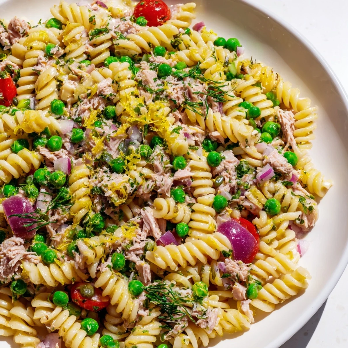 The finished Lemony Tuna Pasta Salad in a glass serving bowl, showcasing fusilli pasta mixed with tender tuna flakes, bright green peas, and finely chopped red onion.