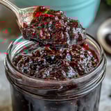 Homemade Black Currant Jam with deep purple color and a jammy, glistening texture, captured in a rustic white bowl.