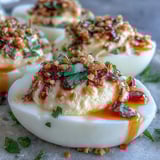 Twelve spicy chili garlic deviled egg halves stacked neatly, showing creamy yolk filling and a glossy oil drizzle.