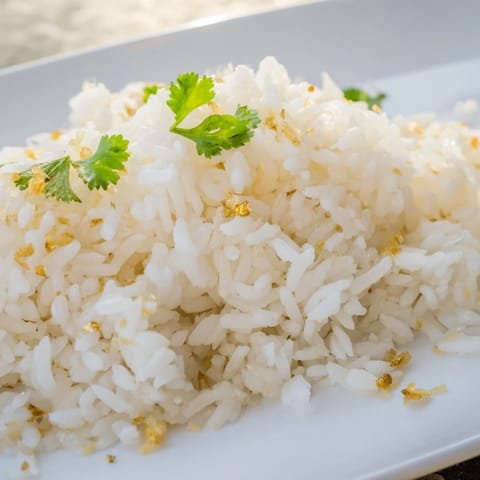 A close-up of fluffy Jasmine Rice Garlic in a white bowl, topped with scallions, beside a stir-fry for serving.
