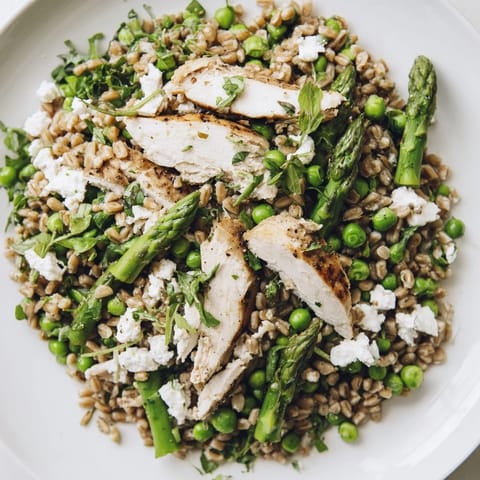 A hearty serving of Warm Spring Farro Chicken Salad features juicy chicken, crisp asparagus, and sweet peas tossed with peppery arugula and a light lemon dressing.