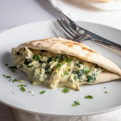 Steam rises from warm pita bread packed with tender chicken, artichoke hearts, and fresh spinach leaves.