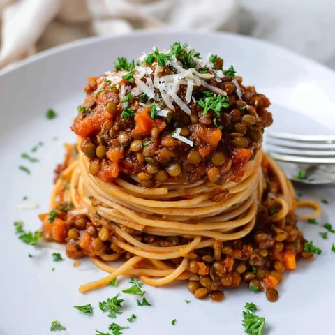 A vibrant bowl of Lentil Bolognese with twirled pasta, fresh herbs, and a rustic wooden background for serving.  