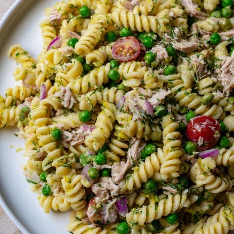 A close-up of Lemony Tuna Pasta Salad glistening with olive oil and lemon zest, garnished with fresh parsley and dill, perfect for a refreshing lunch.