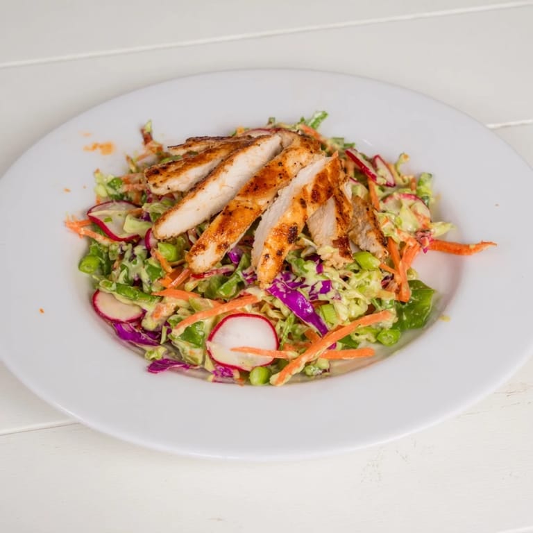 Freshly grilled chicken rests atop bright green Green Goddess Cabbage Slaw, ready to be enjoyed.