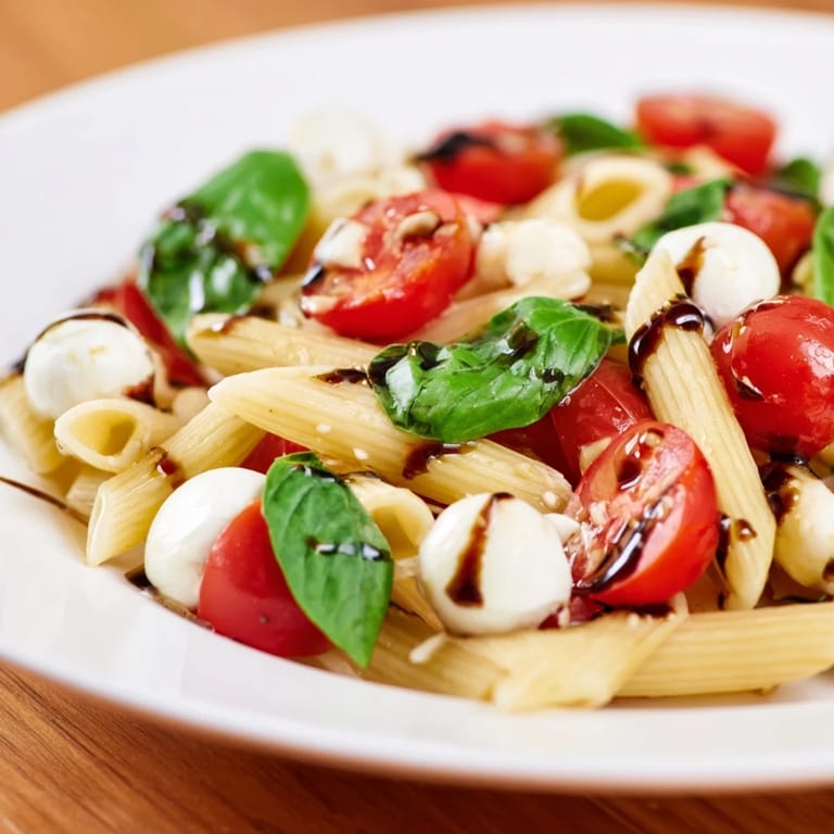 Bright Caprese Salad Pasta is served on a plate, drizzled with balsamic glaze and extra basil leaves for a fresh, summery Italian meal.