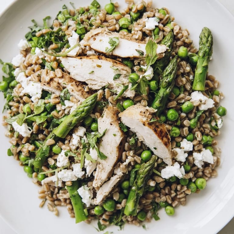 A hearty serving of Warm Spring Farro Chicken Salad features juicy chicken, crisp asparagus, and sweet peas tossed with peppery arugula and a light lemon dressing.