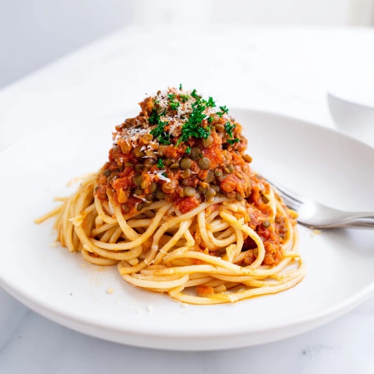 Rich, simmered Lentil Bolognese sauce clinging to al dente spaghetti in a white bowl, topped with fresh basil.