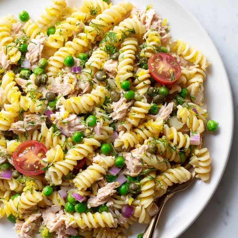 Top-down view of Lemony Tuna Pasta Salad served on a rustic wooden table, featuring colorful ingredients like cherry tomatoes and capers mixed throughout.
