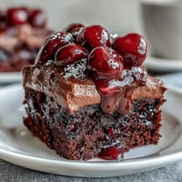 Decadent Cherry Cola Chocolate Poke Cake topped with creamy frosting and cherries.